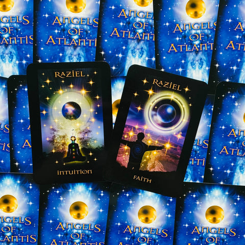 Angelų kortos Angels of Atlantis su mėlynomis nugarėlėmis, dvi atviros Raziel kortos — Intuition ir Faith, kosminis blizgantis dizainas