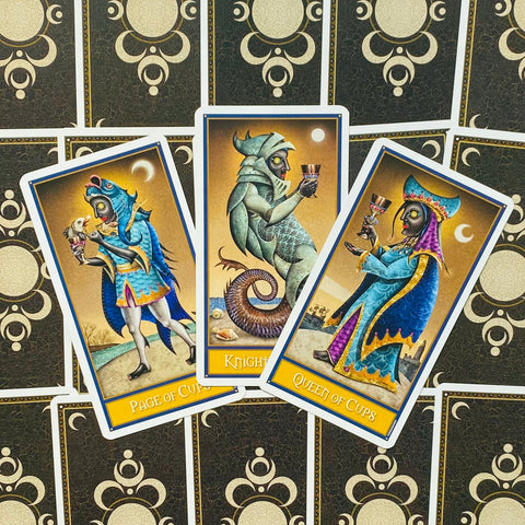 tarot kortos trijų taurų rūšies: Page, Knight ir Queen of Cups su mėlynais‑auksiniais rėmais, išdėstytos ant dekoratyvios nugarėlės fono