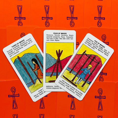 Tarot kortos trijų lazdelės kortų išklotinė ant ryškiai oranžinių nugarėlių su violetiniais ankh simboliais