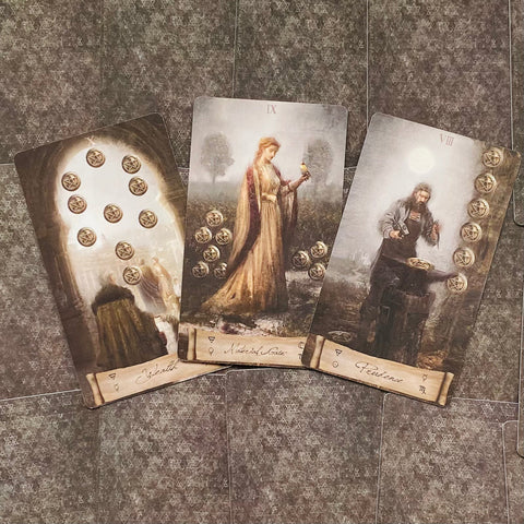 Tarot kortos vintage stiliaus rinkinys su trimis atvertomis Pentaklių kortomis (VIII, IX, X), rodomos iš viršaus ¾ kampu