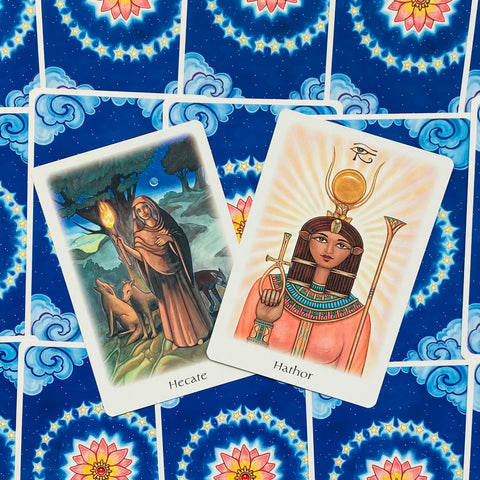 Tarot kortos su Hecate ir Hathor iliustracijomis — priekiniai dievybių variantai ant mėlynos žvaigždėtos nugarėlės, pateiktos pasvirusiu kampu
