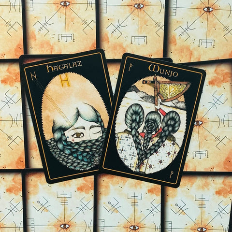 tarot kortos juodais rėmais, dvi atverstos kortos Hagalaz ir Wunjo su pintinėmis kasomis ant simboliško kreminio fono