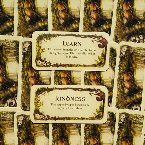 Kortų rinkinys: dvi atverstos "Learn" ir "Kindness" kortelės su šiltomis miško iliustracijomis ir dekoratyviais rėmeliais