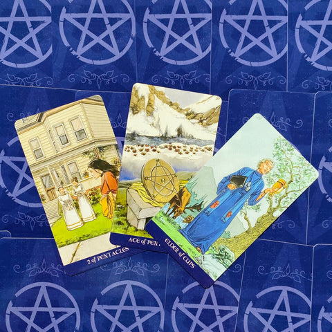 Tarot kortos RWS stiliaus rinkinys, trys atverstos kortos virš mėlynos pentaklio nugarėlės, fanuotas kampu