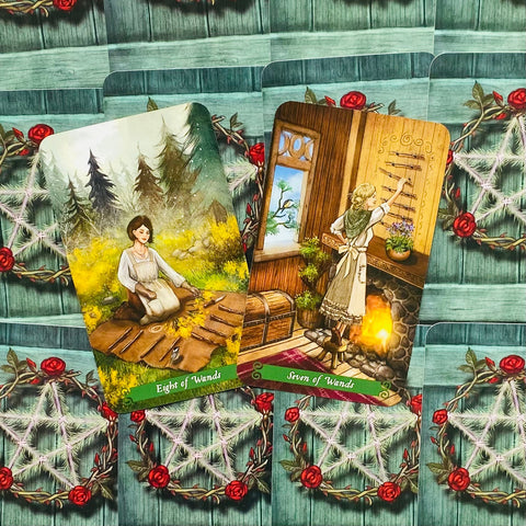 tarot kortos su "Eight of Wands" ir "Seven of Wands" ilustracijomis, šiltos medinės spalvos ir žalia nugarėlė su raudonomis rožėmis
