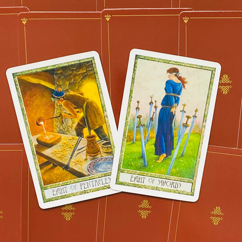 Tarot kortos Rider‑Waite stiliaus rinkinys: dvi atviros kortos (Aštuoni Pentakliai, Aštuoni Kardai) ant raudono ornamentuoto fono, šiek tiek pasvirusios