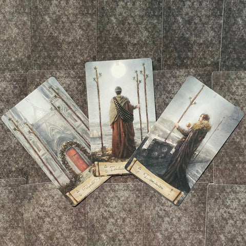 Tarot kortos — trys atverstos kortos su jūros ir pilkšvais peizažais ant tamsaus žvaigždėto nugarėlių fono