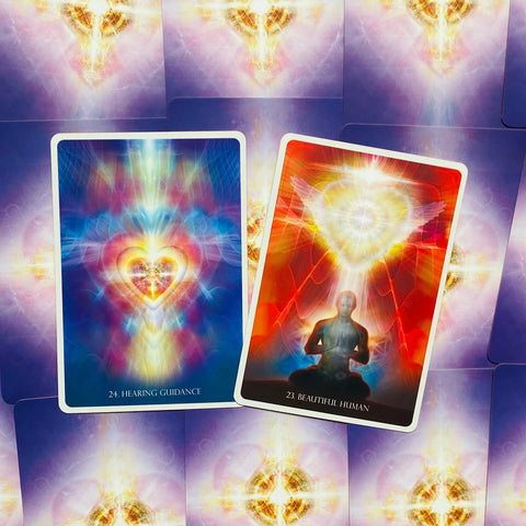 Orakulų kortos: dvi ryškios kortos — mėlyna "Hearing Guidance" ir raudona "Beautiful Human", su meditacinės širdies energijos motyvais ir baltu rėmeliu