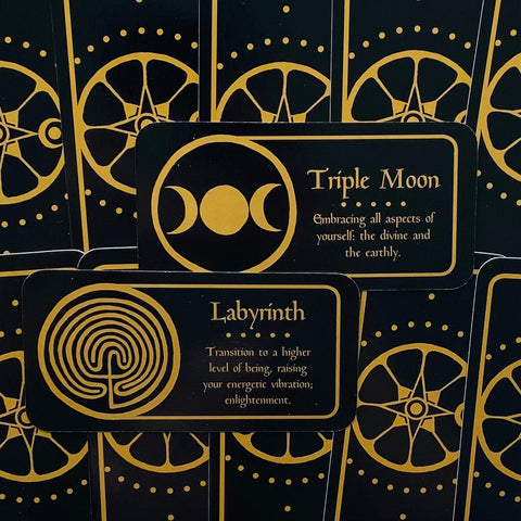 Orakulo kortos juodai auksinės, arti užfiksuotos kortų priekio versijos su Triple Moon ir Labyrinth simboliais bei tekstu