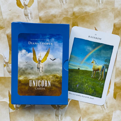 Diana Cooper mėlyna „Unicorn Cards“ dėžutė rodoma iš viršaus su atversta „Rainbow“ korta — auksaspalvė sparnuota vienaragė ir vaivorykštė