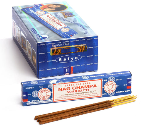 Nag Champa smilkalai Satya, mėlyna 15 g pakuotė su keliomis rudos spalvos lazdelėmis priekyje ir didesne dėžute fone