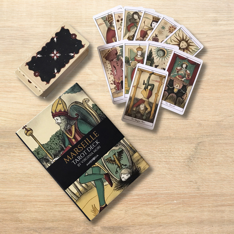 Marseille tarot kortų rinkinys su iliustruota dėžute ir išskleistu kortų vėduoklės išdėstymu ant šviesaus medžio fono, vintage spalvos