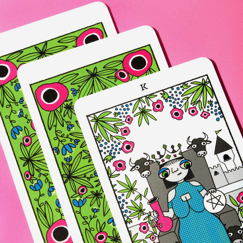 Tarot kortos fanuotos trys kortos, iliustruotas karalius kortoje, ryškios žalios gėlėtos nugarėlės ir rožinis fonas