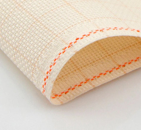 Elastinis tvarstis smėlio spalvos su oranžine siūle, užlenktu kraštu ir grublėta audinio faktūra — arti pabrėžiama siūlių detalė