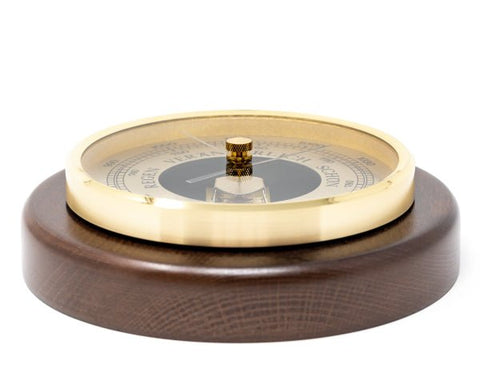 Barometras ant tamsaus medinio pagrindo su žalvariniu žiedu, artimas kampinis planas ir matomas ciferblatas