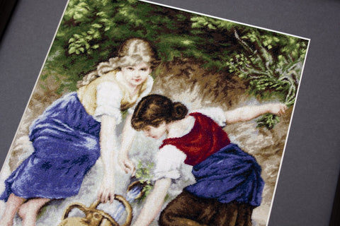 Siuvinėtas paveikslas dvi mergaitės prie upelio, rankų darbo kryželiu, mėlynos ir raudonos spalvos, kampinis artimas kadras
