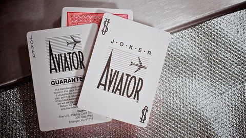 Aviator kortos: dvi baltos Joker kortos sluoksniuotos ant sidabriško tekstūruoto paviršiaus, matomas logotipas