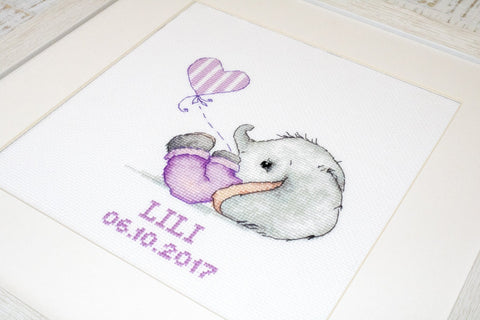 Siuvinėtas paveikslas kūdikiui rėmelyje: pilkas dramblio siluetas ir violetinis širdies balionėlis, personalizuotas vardu LILI ir data 05.10.2017