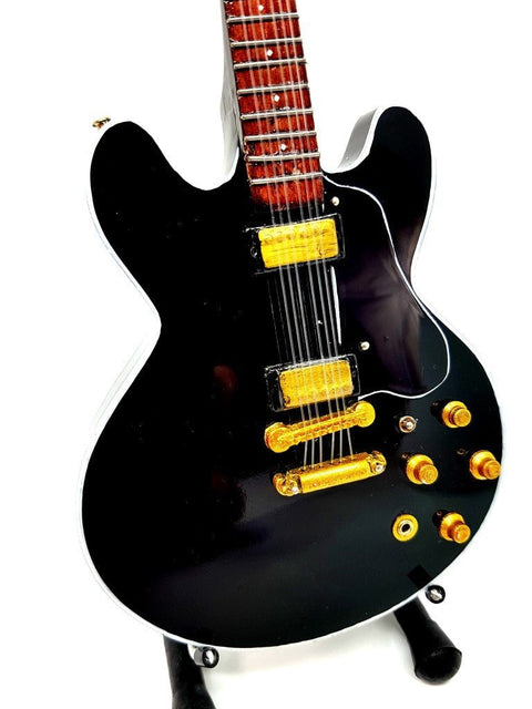 Elektrinė gitara juoda pusiau hollow kūno artimas kadras, akcentuojantis auksinius pickup’us ir valdiklių detales