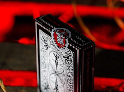 Pokerio kortų kaladė juodo‑raudonos dėžutės, uždarytas kampas su raudona emblema ir ryškiu ornamentu