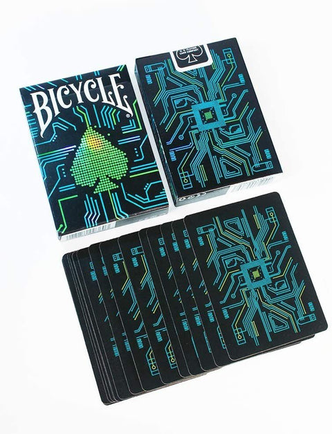 Bicycle kortos su juodu fonu ir neoninėmis mėlynomis bei žaliomis elektroninės plokštės raštų detalėmis, parodytos dvi dėžutės ir atverstos kortos