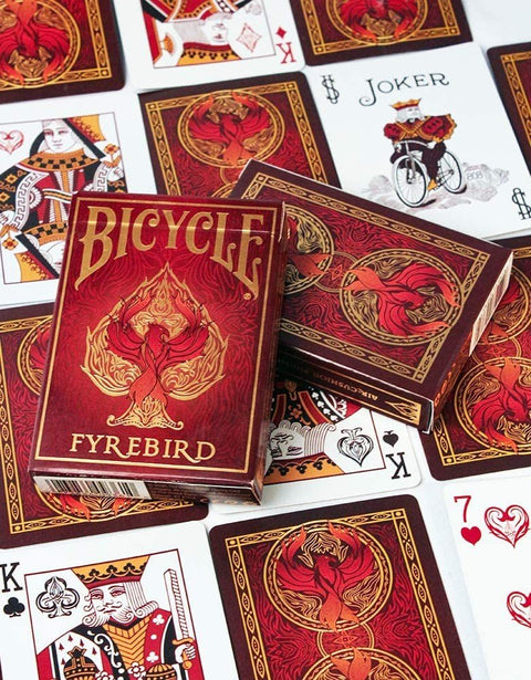 Bicycle Fyrebird žaidimo kortos su raudonu ir auksiniu dėklu bei puošniu ornamentiniu nugarėlių dizainu, dėžutės kampas matomas