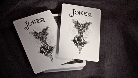 Kortų kaladė Joker juodai baltomis iliustracijomis, dvi persidengiančios Joker kortos viršuje, fotografuota iš kampo