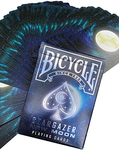 Bicycle kortos Stargazer Moon, mėlyno‑juodo galaktikos dizaino dėžutė priekyje ir išskleistos kortų nugarėlės su mėnuliu