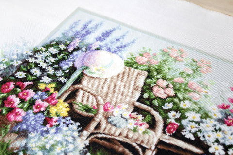 Kryželių siuvinys su pastelinių gėlių ir pintinės vežimėlio motyvu, artimas siūlių ir tekstūros detalėms