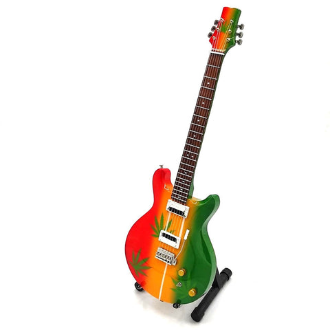 Elektrinė gitara raudona–geltona–žalia su kanapių lapų dizainu, dviem pickupais ir stovėjimo laikikliu, trijų ketvirčių perspektyva