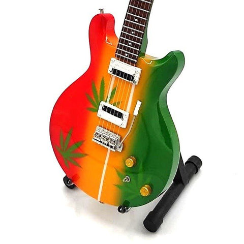 Elektrinė gitara raudona–geltona–žalia su kanapių lapų dekoru ant juodo stovo, kampinė priekinė perspektyva