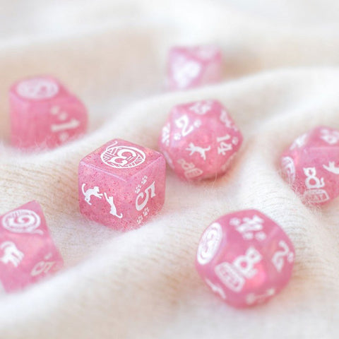 Kauliukai rožiniai RPG rinkinys, 7 vnt., matiniai su baltomis kačiukų piktogramomis, arti nufotografuoti ant švelnaus vilnos fono