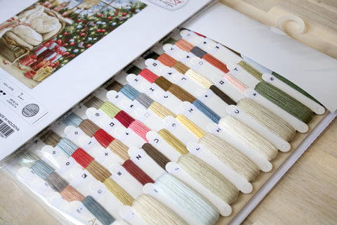 Siuvinėjimo siūlai spalvų kortelėje: įvairių smėlio, žalių, raudonų ir pastelių atspalvių bobinėlės su simboliais, artimas planas