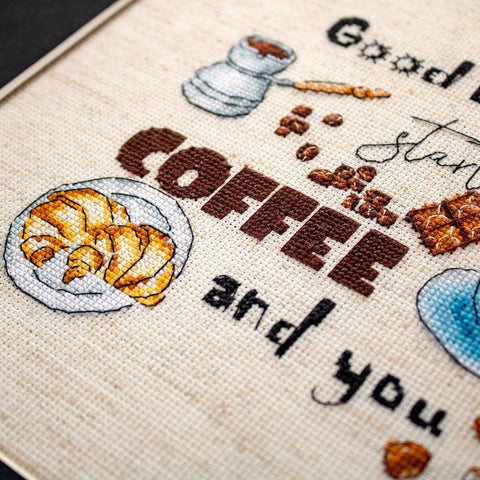 Kryželių siuvinys, arti fiksuota tekstūra ir rudos „COFFEE“ raidės su kruasanu ant baltos lėkštelės ir kavos pupelėmis