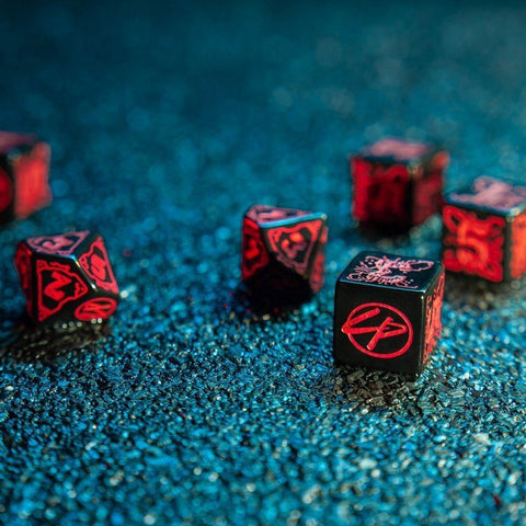 RPG kauliukai juodi su raudonomis graviruotėmis, 6 vnt. komplektas, arti fotografuoti ant mėlyno tekstūruoto paviršiaus