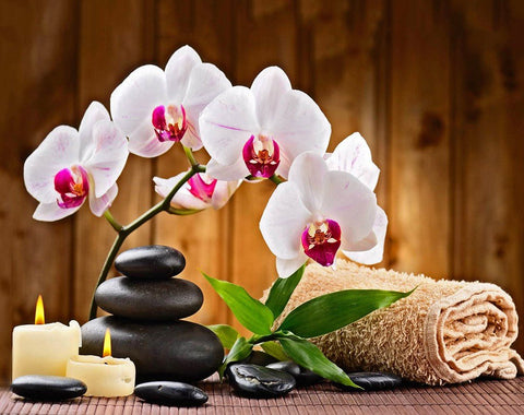 Orchidėja baltai‑rožinė su juodais masažo akmenimis, degančiomis žvakėmis ir susuktu rankšluosčiu, stilinga SPA kompozicija