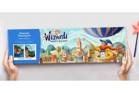 Diamond painting rinkinys Wizardi 38×48 cm su spalvota miestelio ir burbulų žiobro iliustracija, dėžutė priekiniame plane rankose