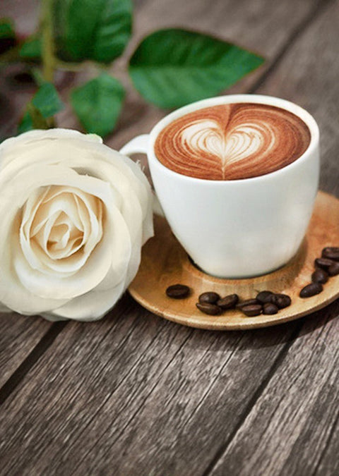 Kava kapučino baltame puodelyje su širdies latte art ant medinio padėklo, šalia baltos rožės dekoracija