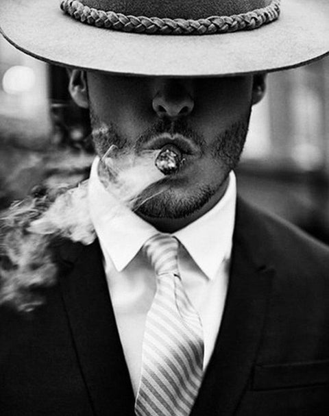 Parduotuvės skrybėlės puslapyje: trijų ketvirčių priekinis kadras – smėlio spalvos fedora su pintu dirželiu, matomas kostiumas ir cigaras, unikalus vyriškas stilius