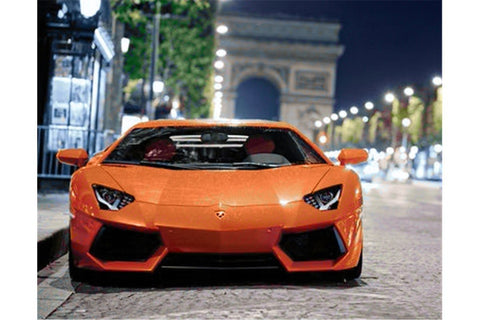 Lamborghini oranžinis sportinis automobilis iš priekio naktinėje Paryžiaus gatvėje prie Triumfo arkos