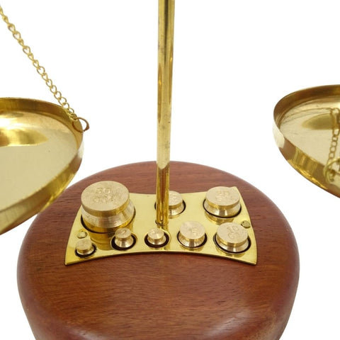Svarstyklės su auksinio žalvario lėkštėmis ir medine baze, rodomi komplekte esantys mažieji kalibruoti svoriai