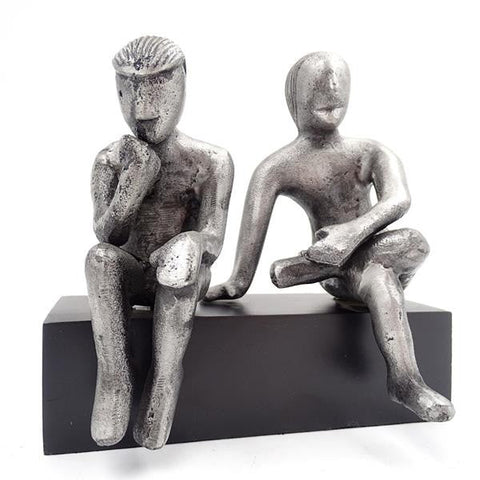 Statuetė modernaus sidabro tonų, dvi abstrakčios sėdinčios figūros ant juodo stačiakampio pagrindo, priekinė perspektyva