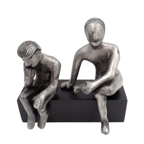 dekoracija: sidabrinės dvi sėdinčios figūros ant juodo stačiakampio pagrindo, priekinis kampas akcentuoja detales ir proporcijas