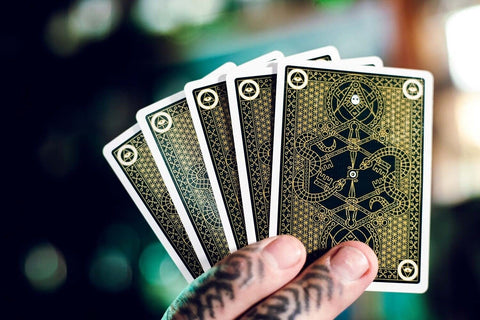 Kortos juodo su aukso ornamentu nugarėle, fanuotos tatuiruotos rankos delne, pabrėžta išsami galinė dizaino versija