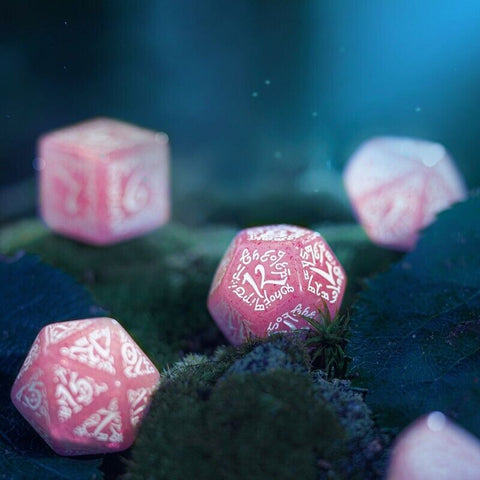 d20 kauliukai rožiniai marmuriniai su baltomis graviruotomis runomis, artimas kampas ant samanų fono, subtili blizgi apdaila