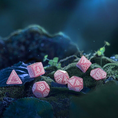 RPG kauliukų rinkinys rožinis su baltais raižiniais, 7 dalių komplektas ant samanų fono, užfiksuotas arti