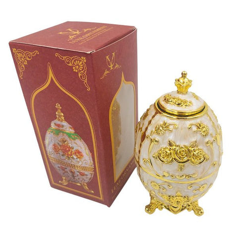 Dekoratyvinis kiaušinis baltas su auksiniais ornamentais ir kojelėmis, elegantiškai pateiktas kartu su raudona dovanų dėže