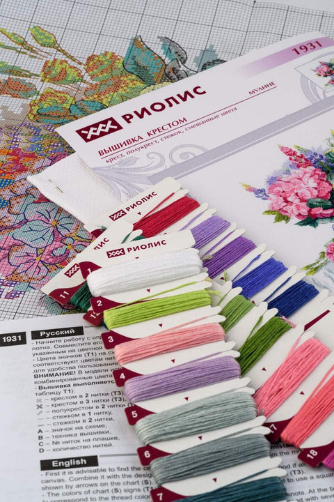Kryželių siuvinėjimo rinkinys Riolis su spalvotų siūlų kortelėmis, detalia instrukcija ir spalvota schema, rodoma siūlų paletė ant audinio