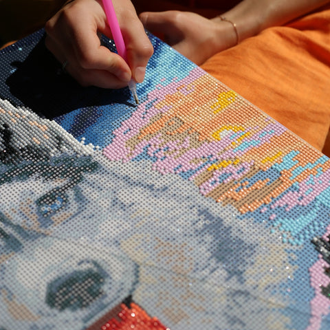 Deimantinė mozaika su vilko motyvu, ranka deda pastelines rožines ir mėlynas kristalines plyteles, rodoma artima darbo detalė