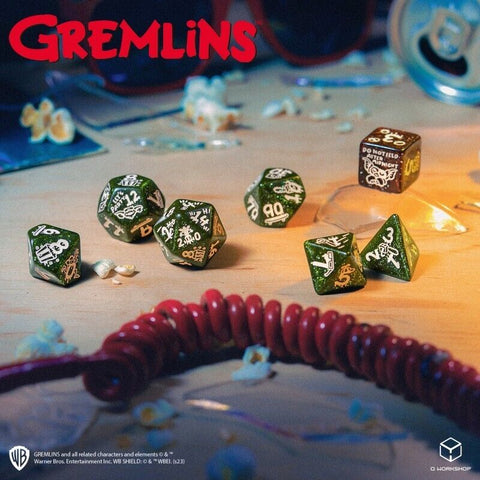 Gremlins kauliukų rinkinys — žali blizgantys 7 polyhedral kauliukai ant medinio stalo, fone raudonas telefono kabelis ir spragėsiai